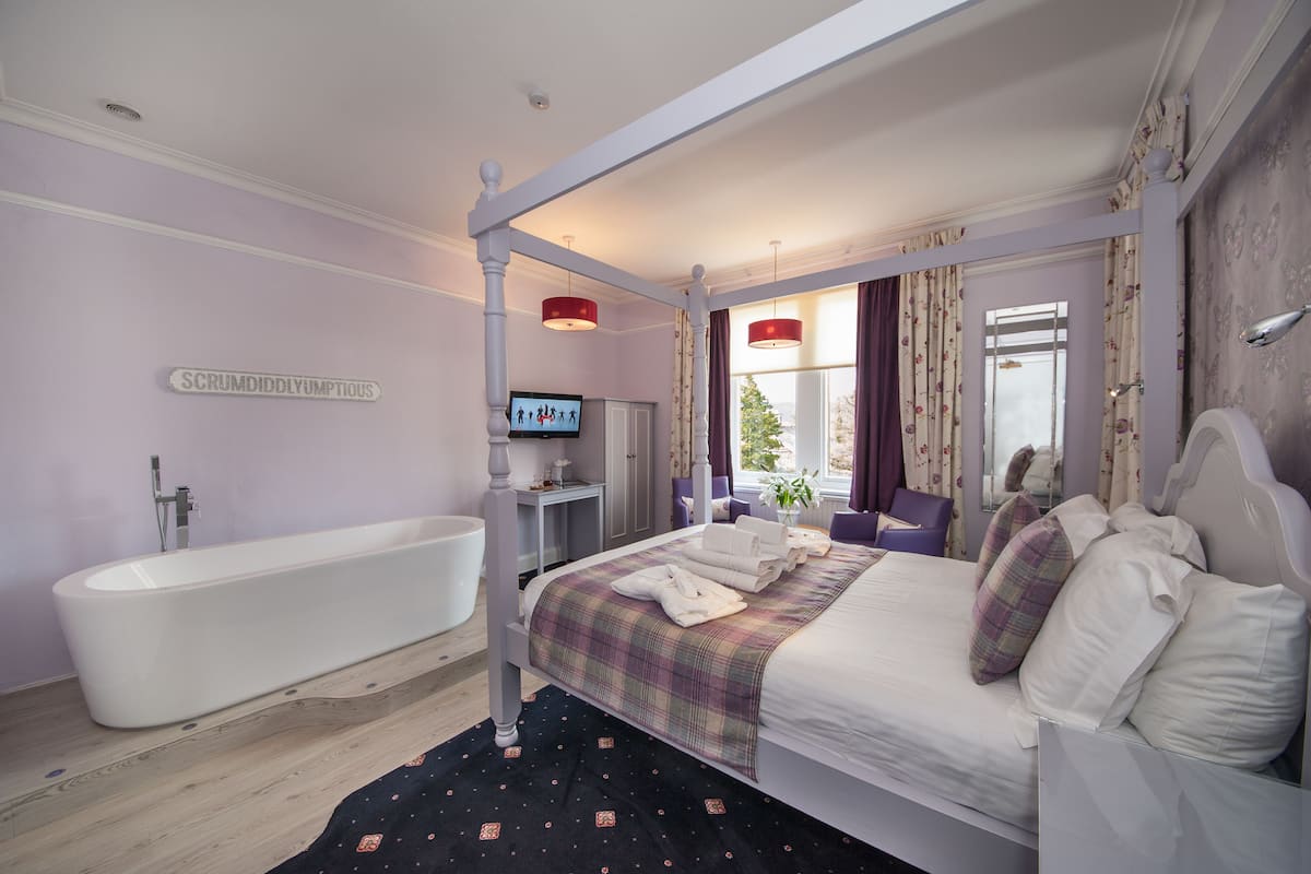 A bedroom with a four-poster bed, a bathtub, and a television on a stand.