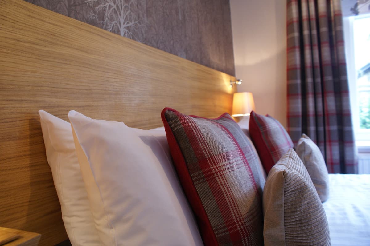 A bed with white and plaid pillows, a wooden headboard, and a lamp on a bedside table.