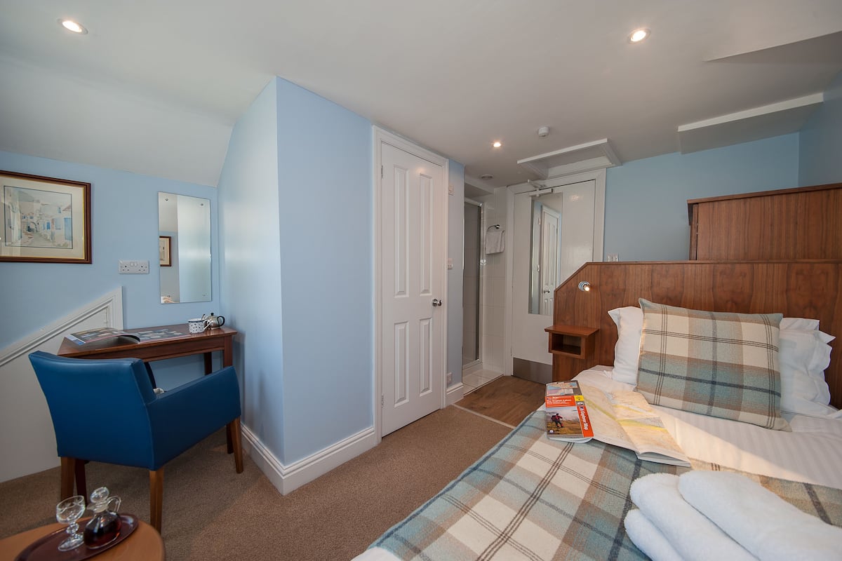 A bedroom with a bed, a desk, and a chair. There is a door leading to another room.