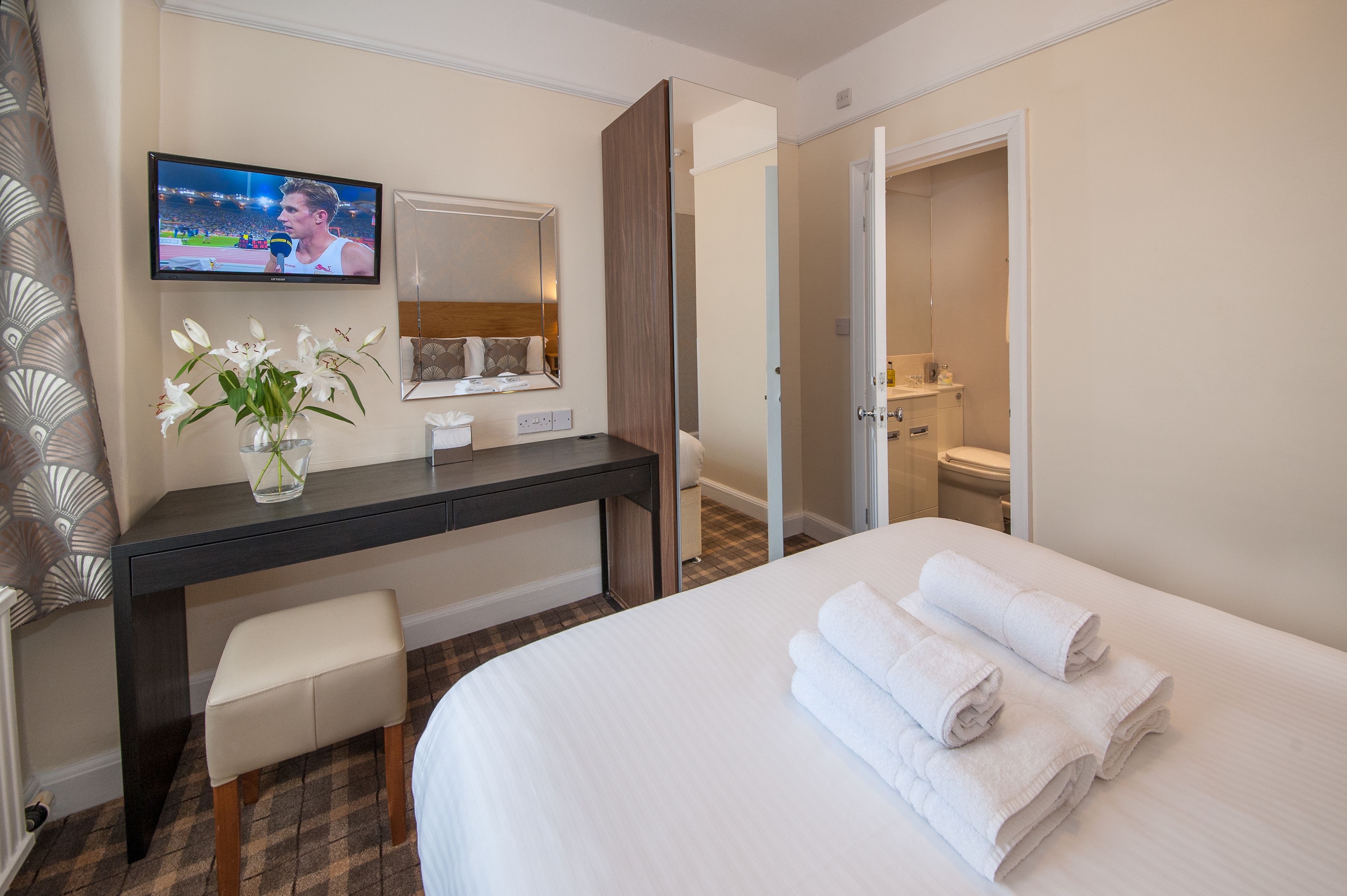 Une chambre d’hôtel avec un lit, un bureau doté d’un miroir, une télévision et une salle de bain visible à travers une porte ouverte.