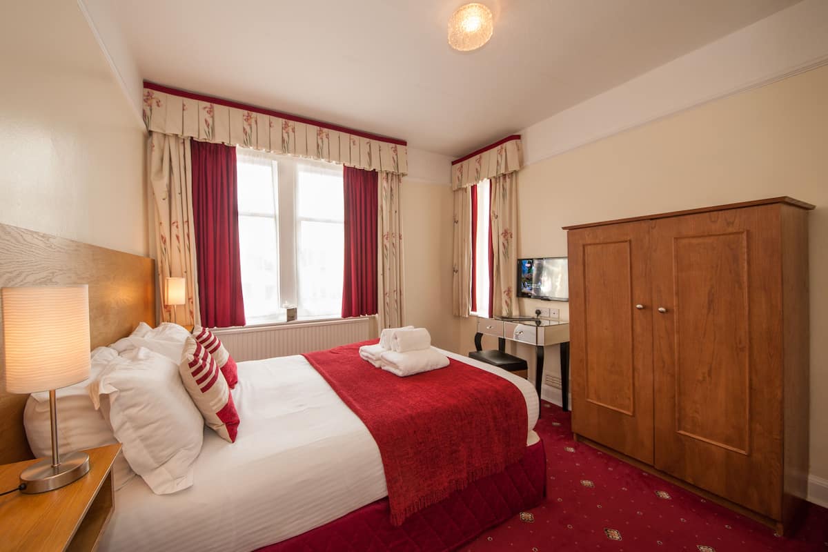 A hotel room with a bed, a desk, a wardrobe, and a mirror.