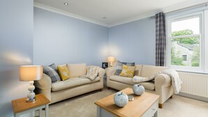 Una sala de estar con un sofá color beige, una mesa de centro de madera y una lámpara sobre una mesita auxiliar.