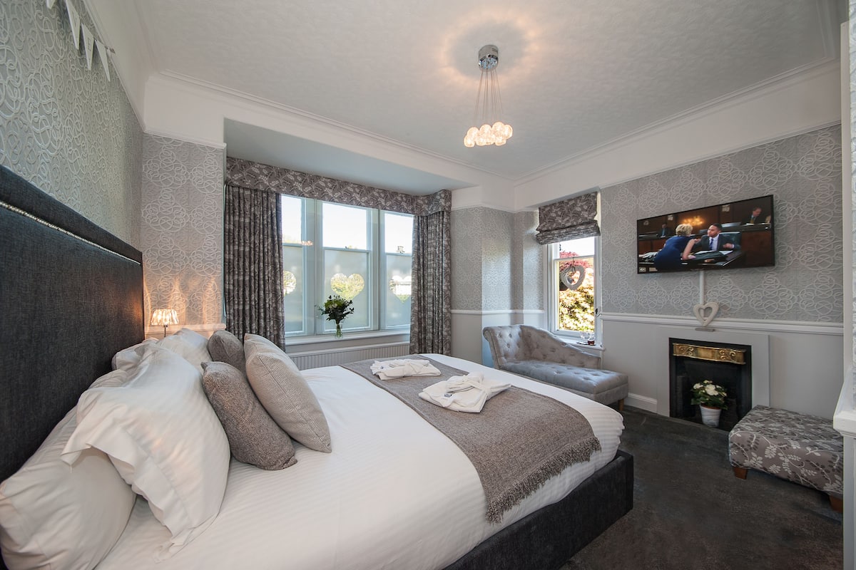 A hotel room with a large bed, a television, a fireplace, and a window with curtains.