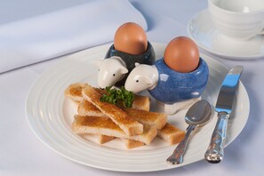 Een bord met brood, een lepel, een mes en twee keramieken eieren met dierenfiguren.