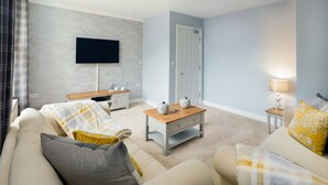 Una sala de estar con un sofá, una mesa de centro, un televisor montado en la pared y una puerta.