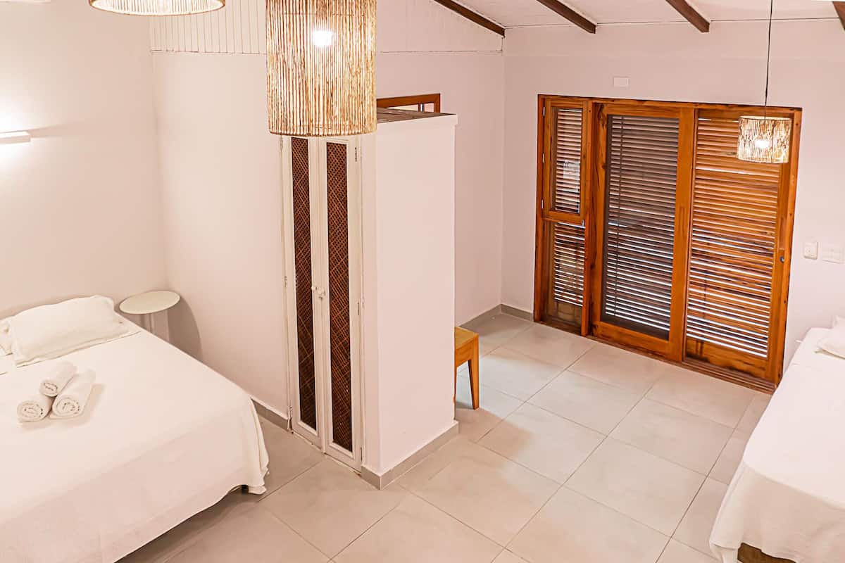 Habitación de hotel con cama, una mesita, una silla, armario y lámpara colgante.