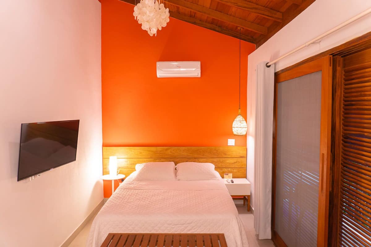 Un dormitorio con cabecera de madera, un televisor de pantalla plana en la pared, una mesita de noche con lámpara y una puerta de cristal corredera.