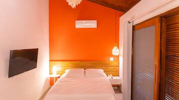 Un dormitorio con cabecera de madera, un televisor de pantalla plana en la pared, una mesita de noche con lámpara y una puerta de cristal corredera.