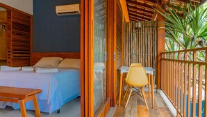 A room with a bed, a table, and a chair, a balcony with a railing, and a view of greenery. - Pousada Jamboo (Ubatuba)
