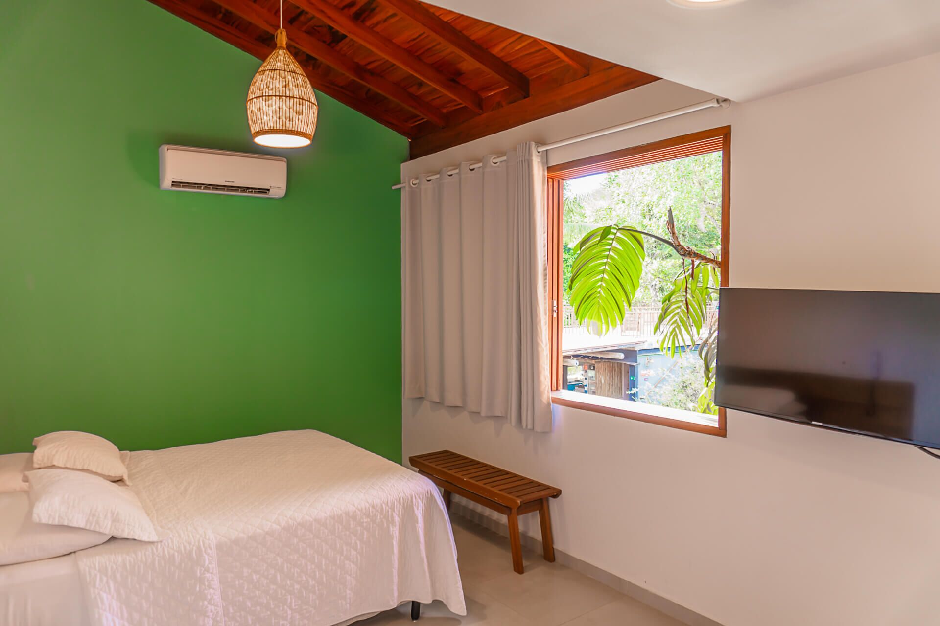 Un dormitorio con cama, una banca, un televisor y una ventana con cortinas.