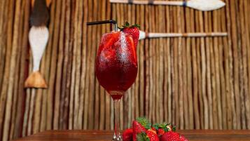 A glass of red drink with a straw and a strawberry garnish, accompanied by fresh strawberries on a wooden table.