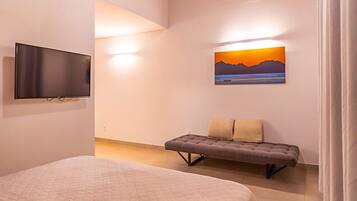 A bedroom with a bed, a bench, a TV, and a sunset painting on the wall.