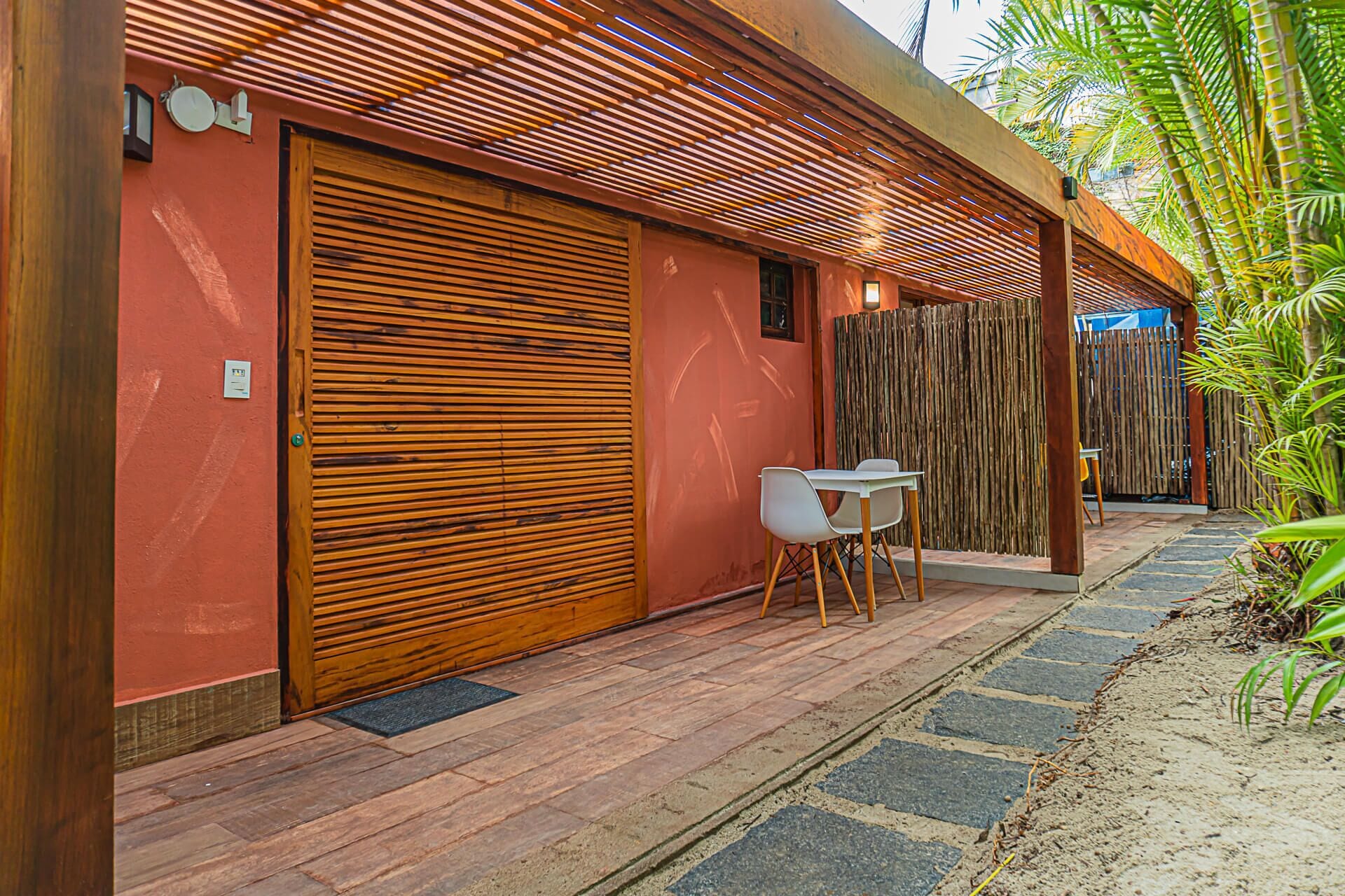 A modern building with a large wooden shutter door, a small table with chairs, and a bamboo fence.