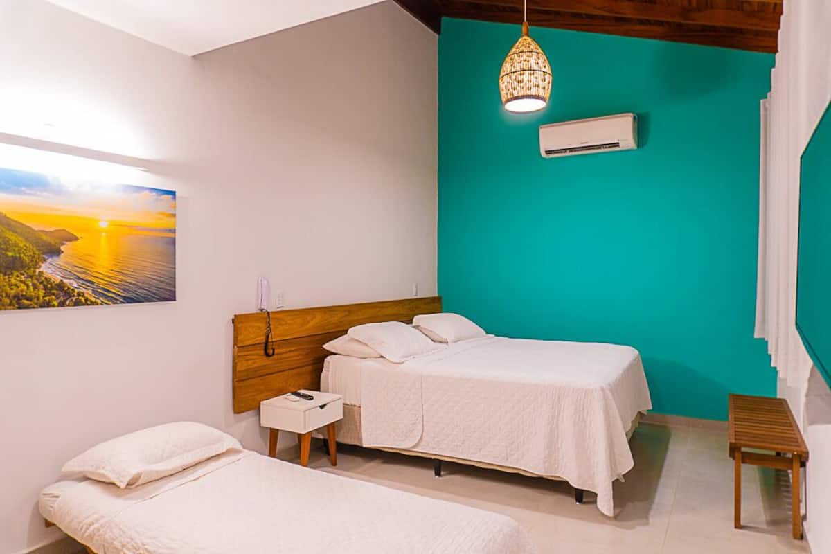 Un dormitorio con dos camas, cabeceros de madera, una mesita de noche, una lámpara colgante y un aire acondicionado de pared.