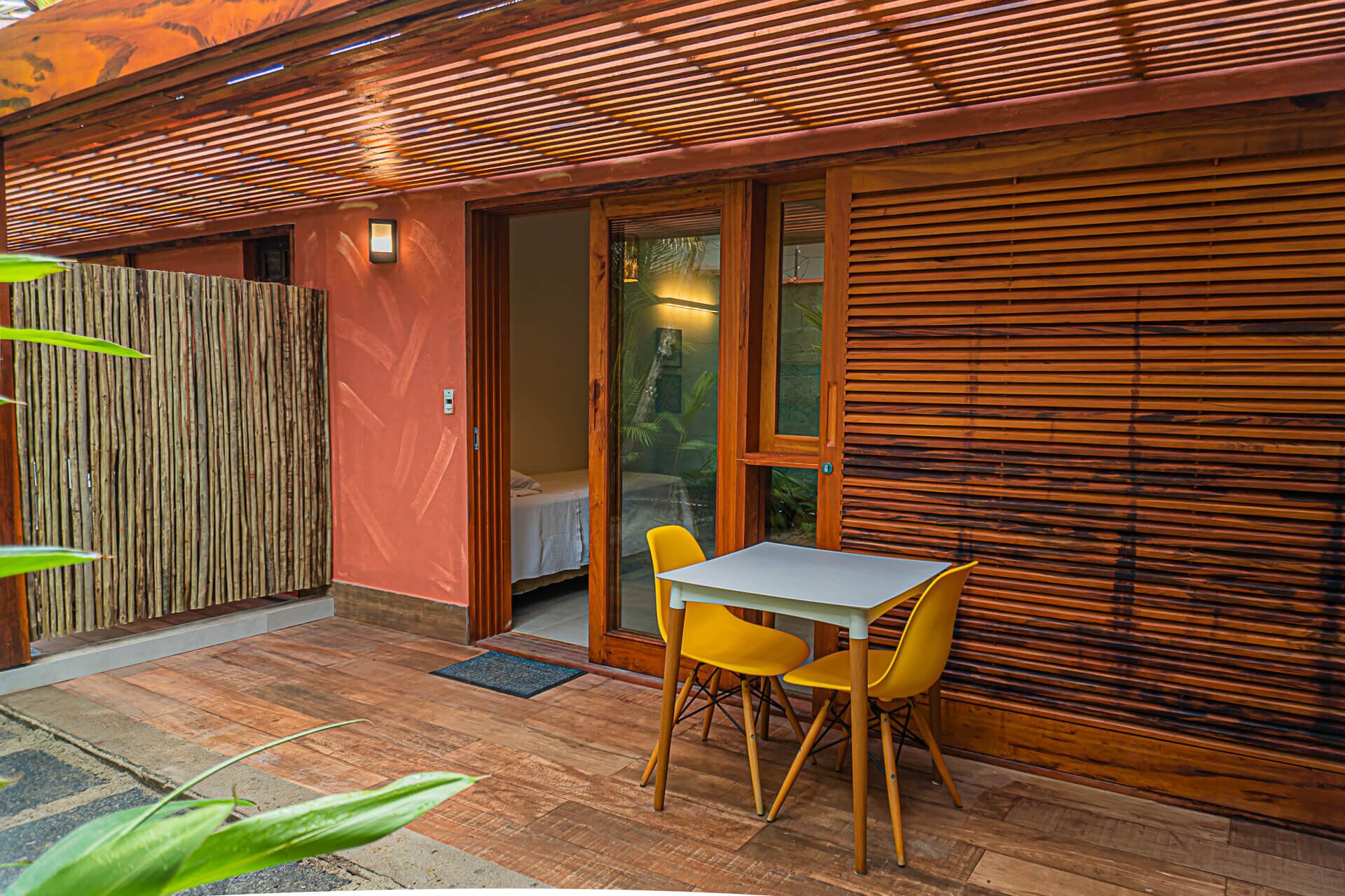 Een terras buiten met een tafel, stoelen, een houten omheining en een schuifdeur die naar een kamer leidt.