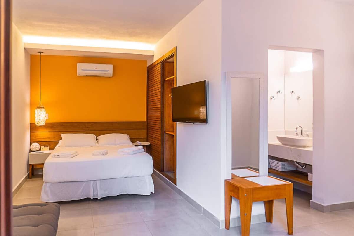 Habitación de hotel con cama, mesita de noche, televisión y baño con lavamanos y espejo.