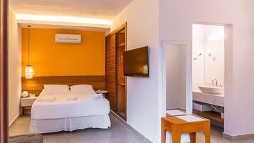 A hotel room with a bed, bedside table, TV, and a bathroom with a sink and mirror.
