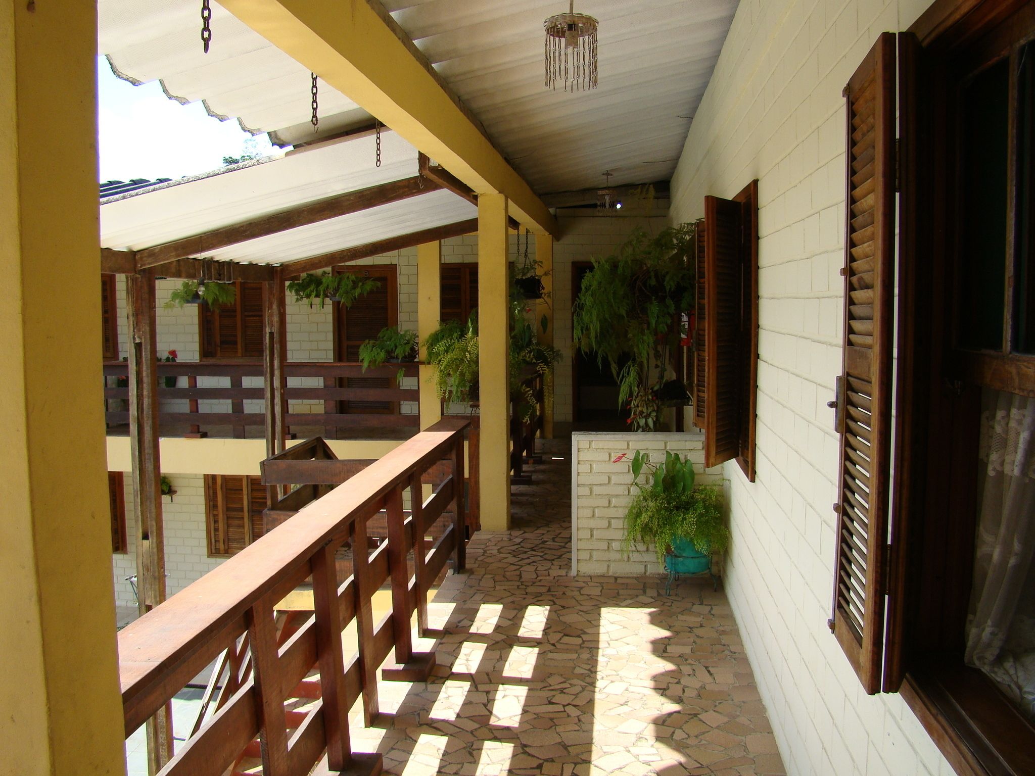 A covered outdoor area with wooden benches, potted plants, and a brick floor.