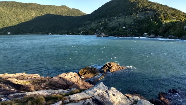 A coastal landscape with rocky shores and a mountain in the background. - Aquarius Chalés (Ubatuba)