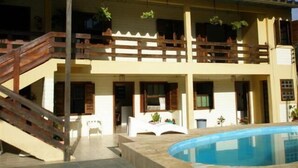 A two-story building with a pool, wooden balconies, and a staircase leading to the upper floor. - Aquarius Chalés (Ubatuba)