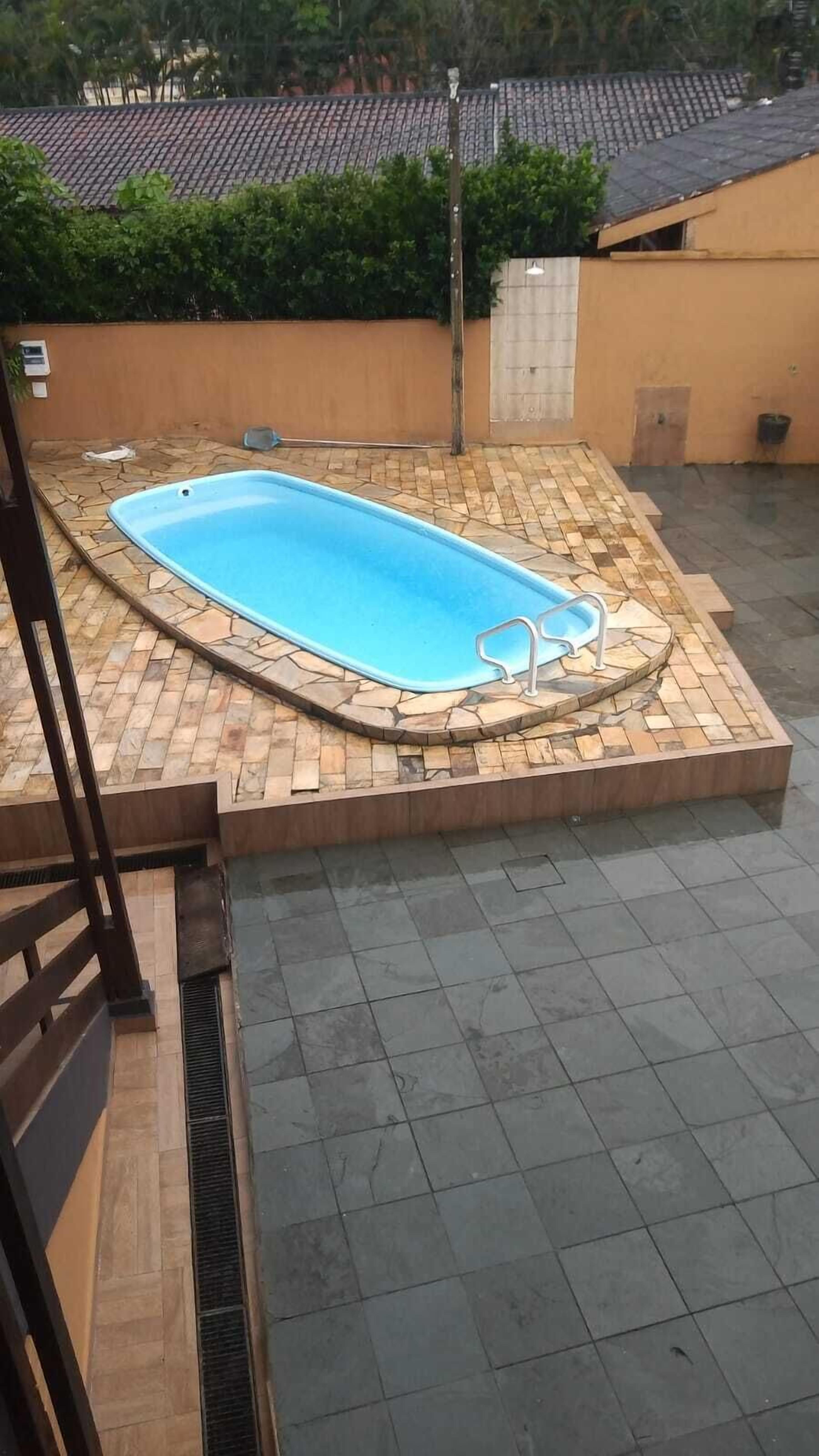 A rectangular swimming pool with a tiled deck, surrounded by a low brick wall and a metal fence.