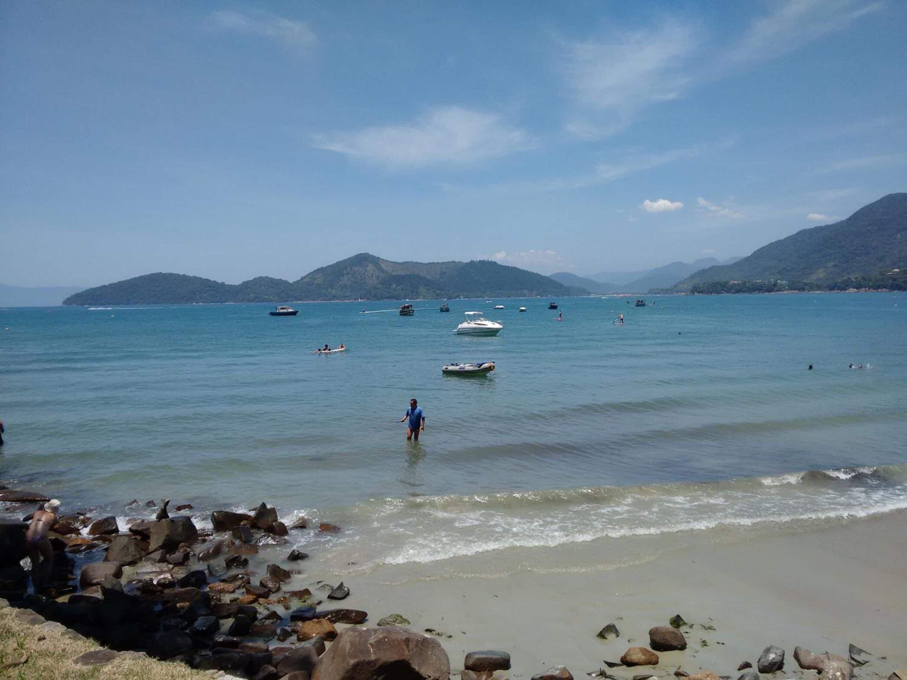 Een strand met boten, een rotsachtige kustlijn en bergen op de achtergrond.