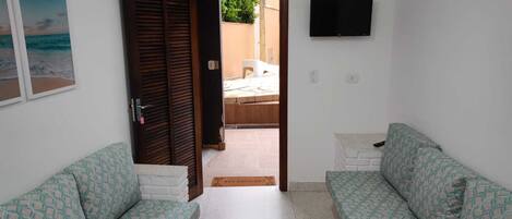 Una habitación con dos sofás estampados, una mesa de centro negra, un televisor montado en la pared y una puerta que da a un espacio al aire libre.