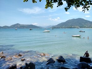 Paisaje costero con barcos en aguas tranquilas, costa rocosa y montañas al fondo.