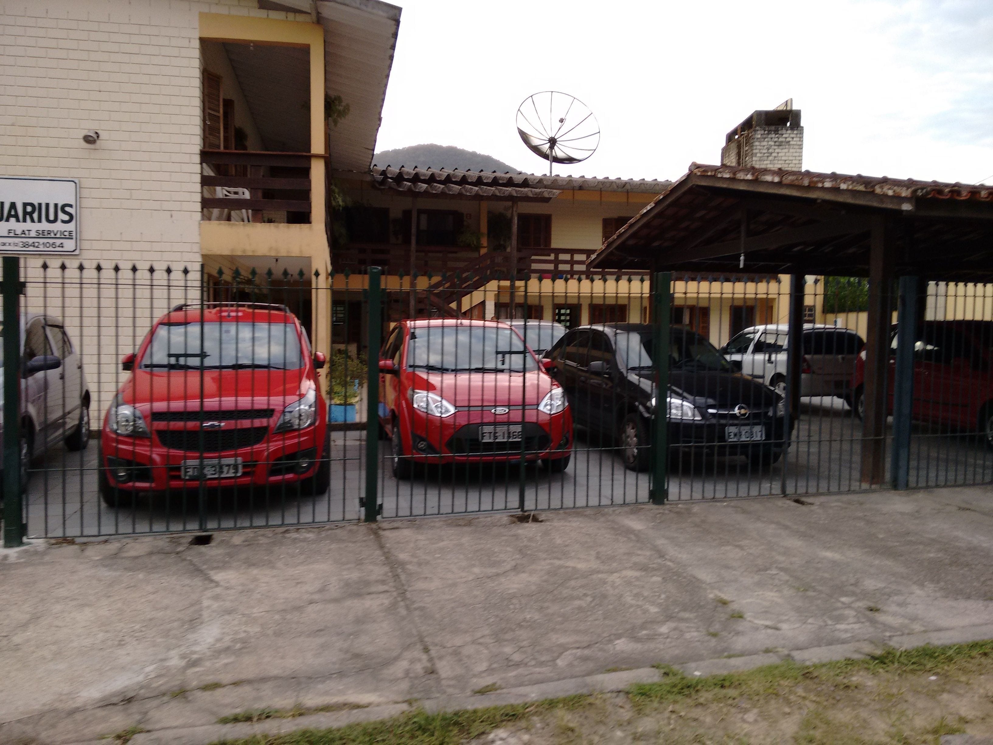 A gated parking area with several cars parked in front of a building with a satellite dish.