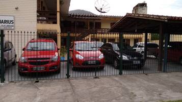 A gated parking area with several cars parked in front of a building with a satellite dish.