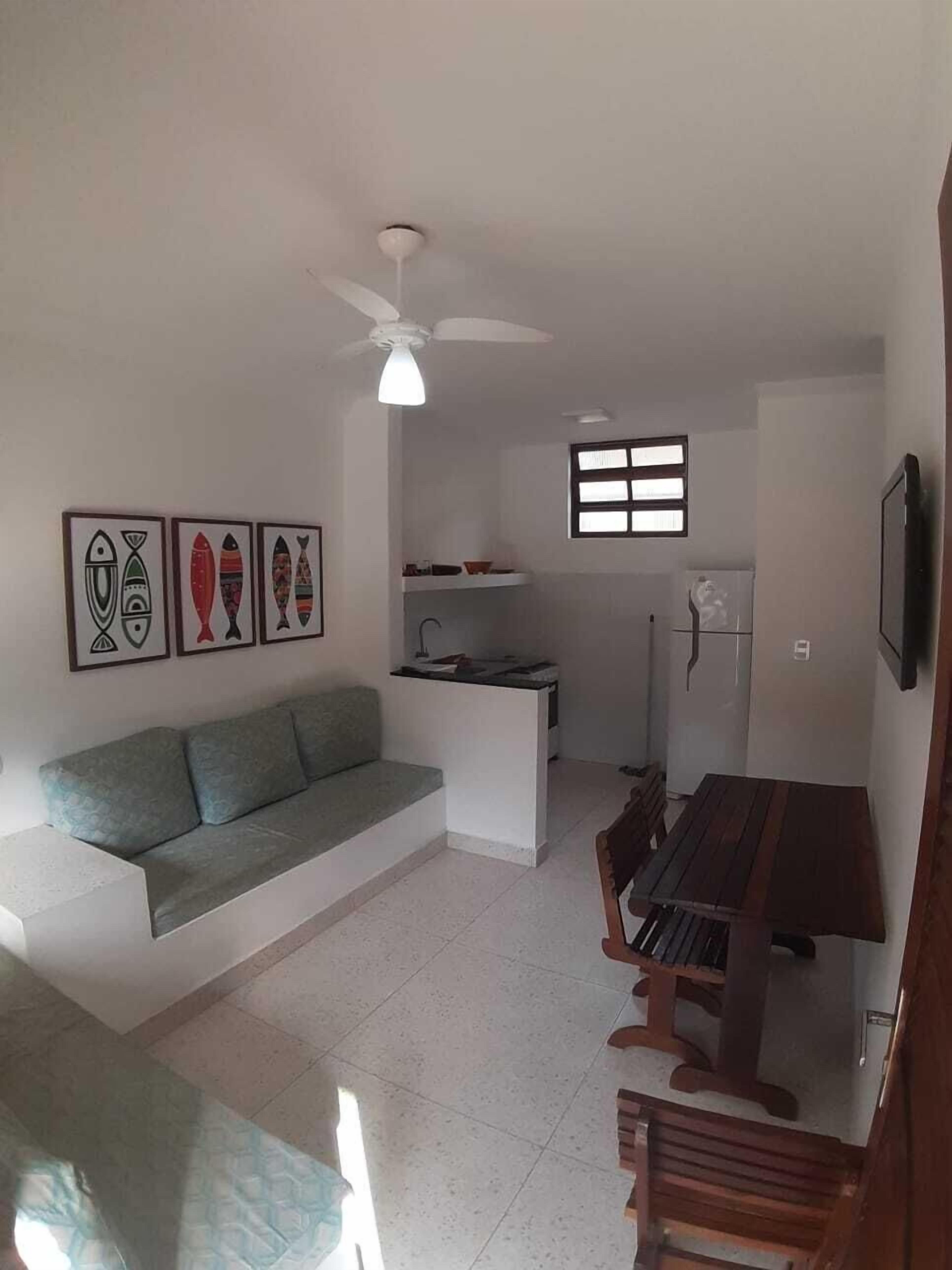 Een ruimtelijk ingerichte leefruimte met een bank, een eettafel met stoelen, een kitchenette en een plafondventilator.