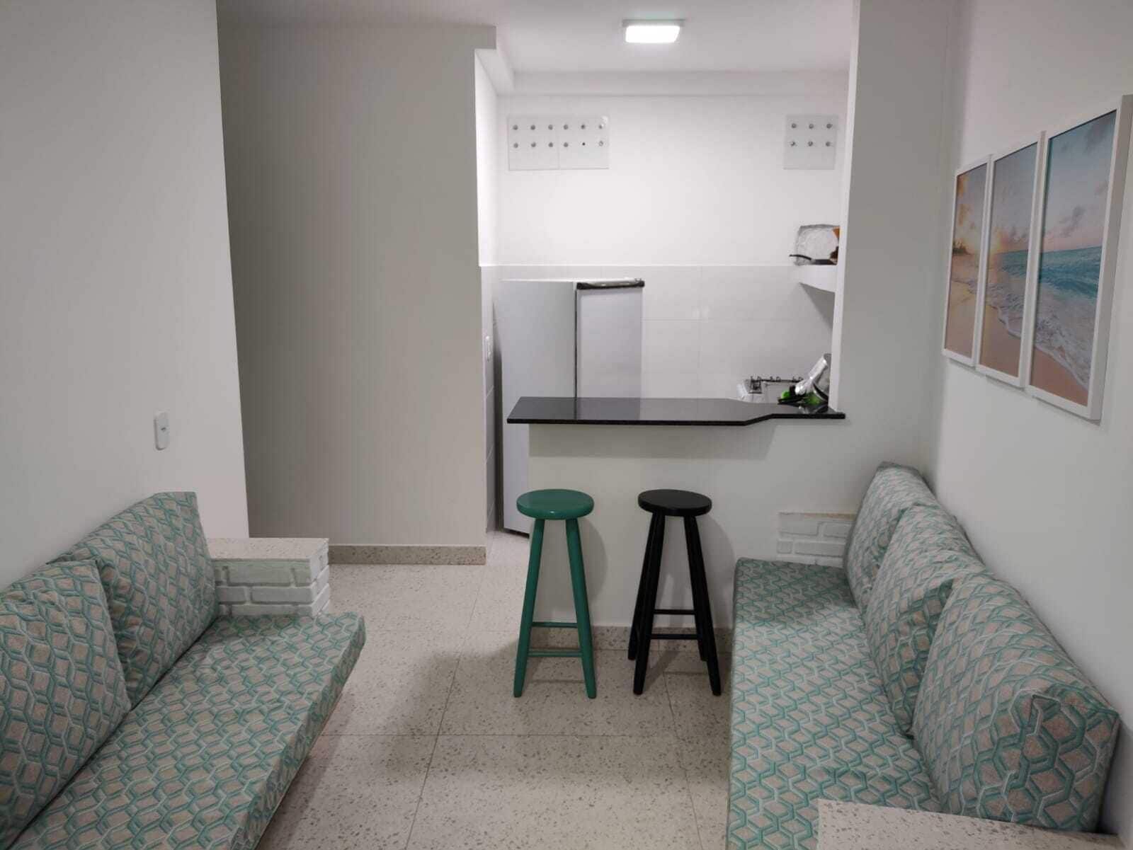 A compact living space with a kitchenette, two stools, and patterned sofas.
