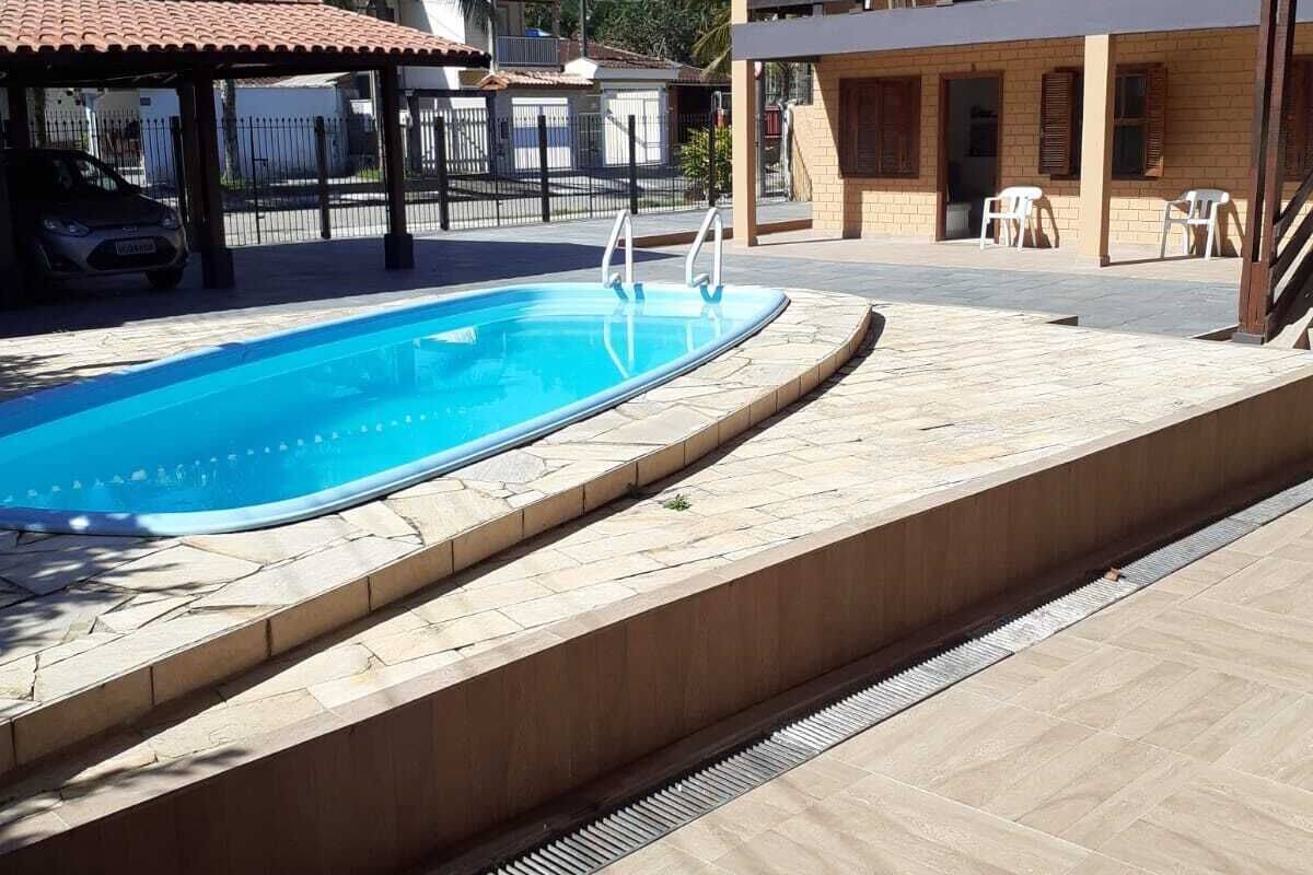 Ein Schwimmbecken mit einer Steindeck, einem überdachten Sitzbereich und einem Gebäude mit Balkon.
