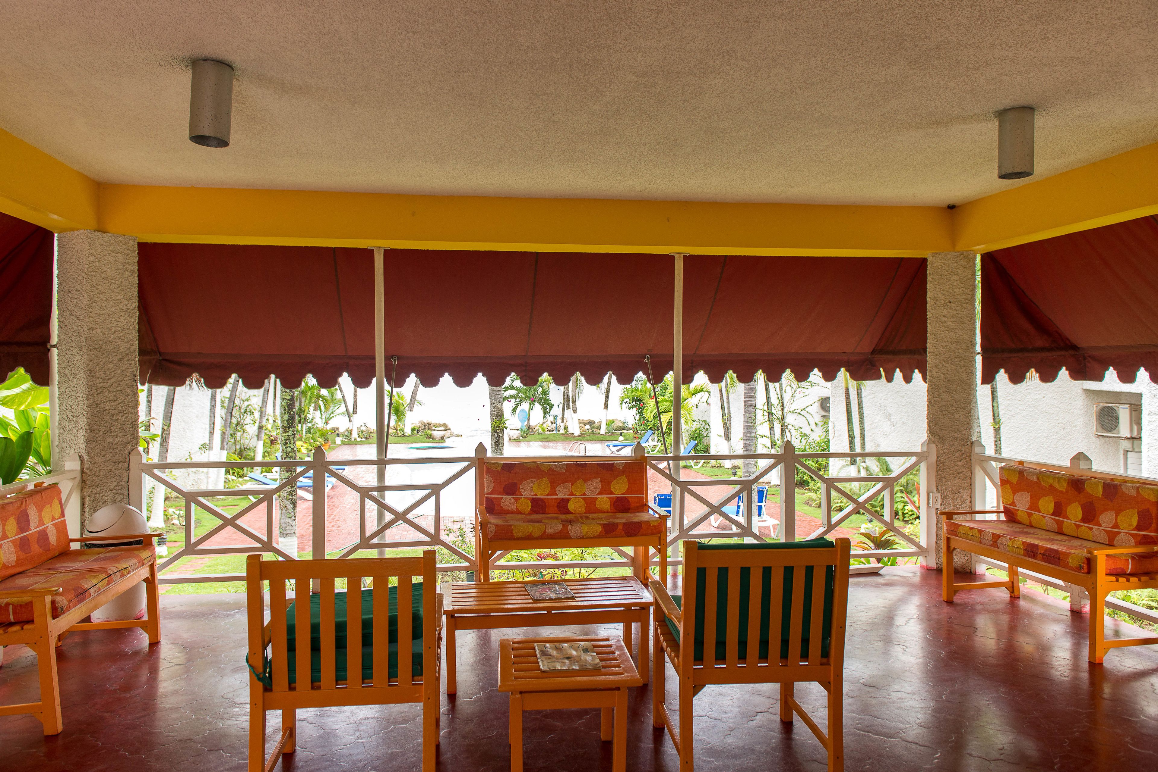 A covered outdoor seating area with wooden furniture and a view of the garden.