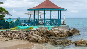 A gazebo with a red roof and blue accents, overlooking a rocky shoreline and calm sea.