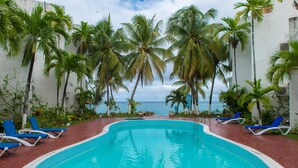 A swimming pool with blue water, surrounded by palm trees and blue lounge chairs.