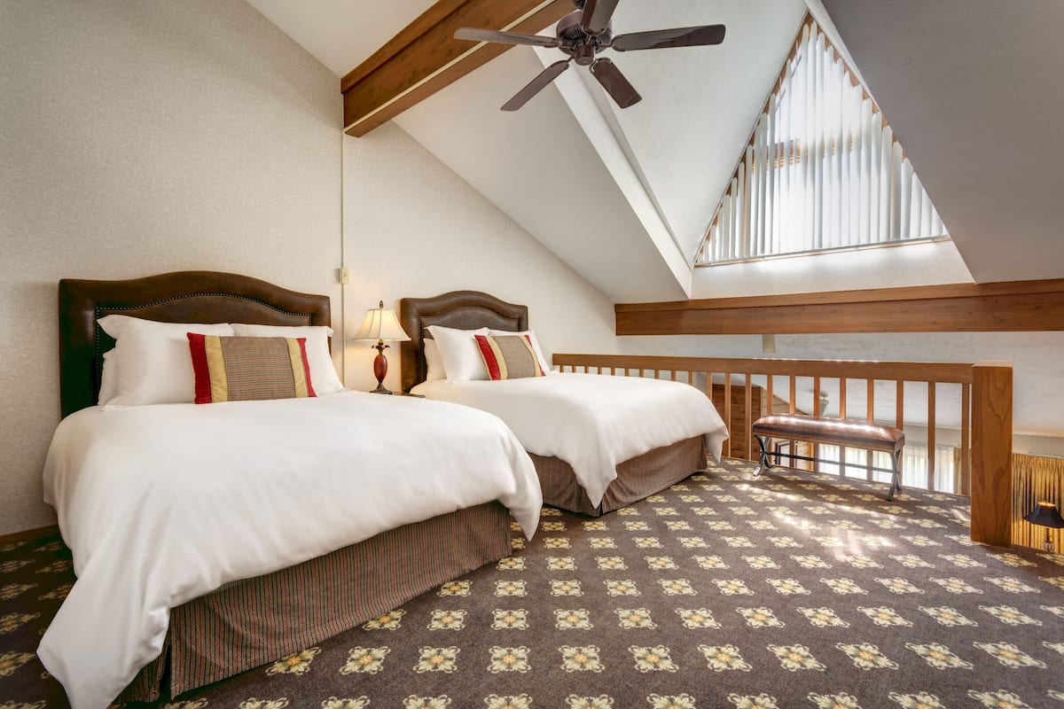 Ein Schlafzimmer mit zwei Betten, einem Deckenventilator, einer Bank und einem gemusterten Teppich.