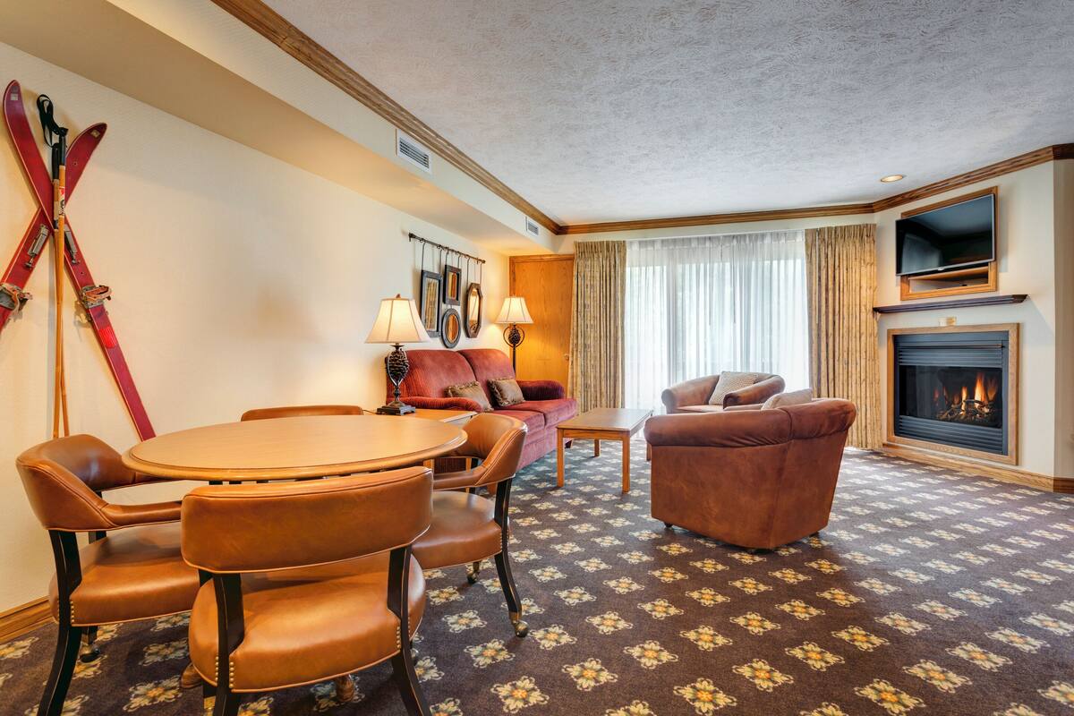 Ein Hotelzimmer mit Esstisch, Stühlen, einer Couch, einem Kamin und Skiern an der Wand.