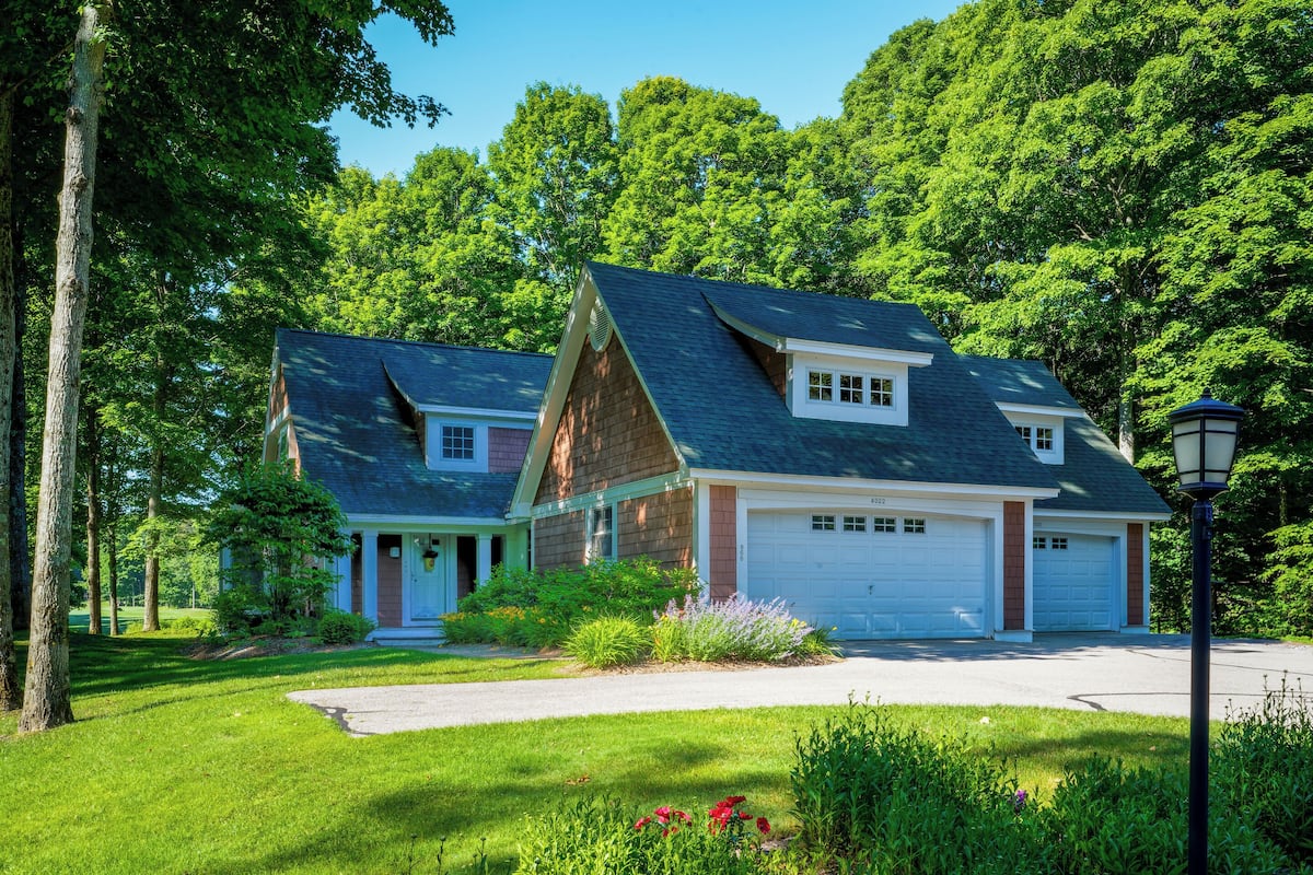 Ein zweistöckiges Haus mit Garage, umgeben von üppigem Grün und Bäumen.