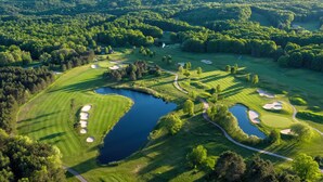 Vista aérea de un campo de golf con múltiples bunkers, un estanque y colinas boscosas circundantes.