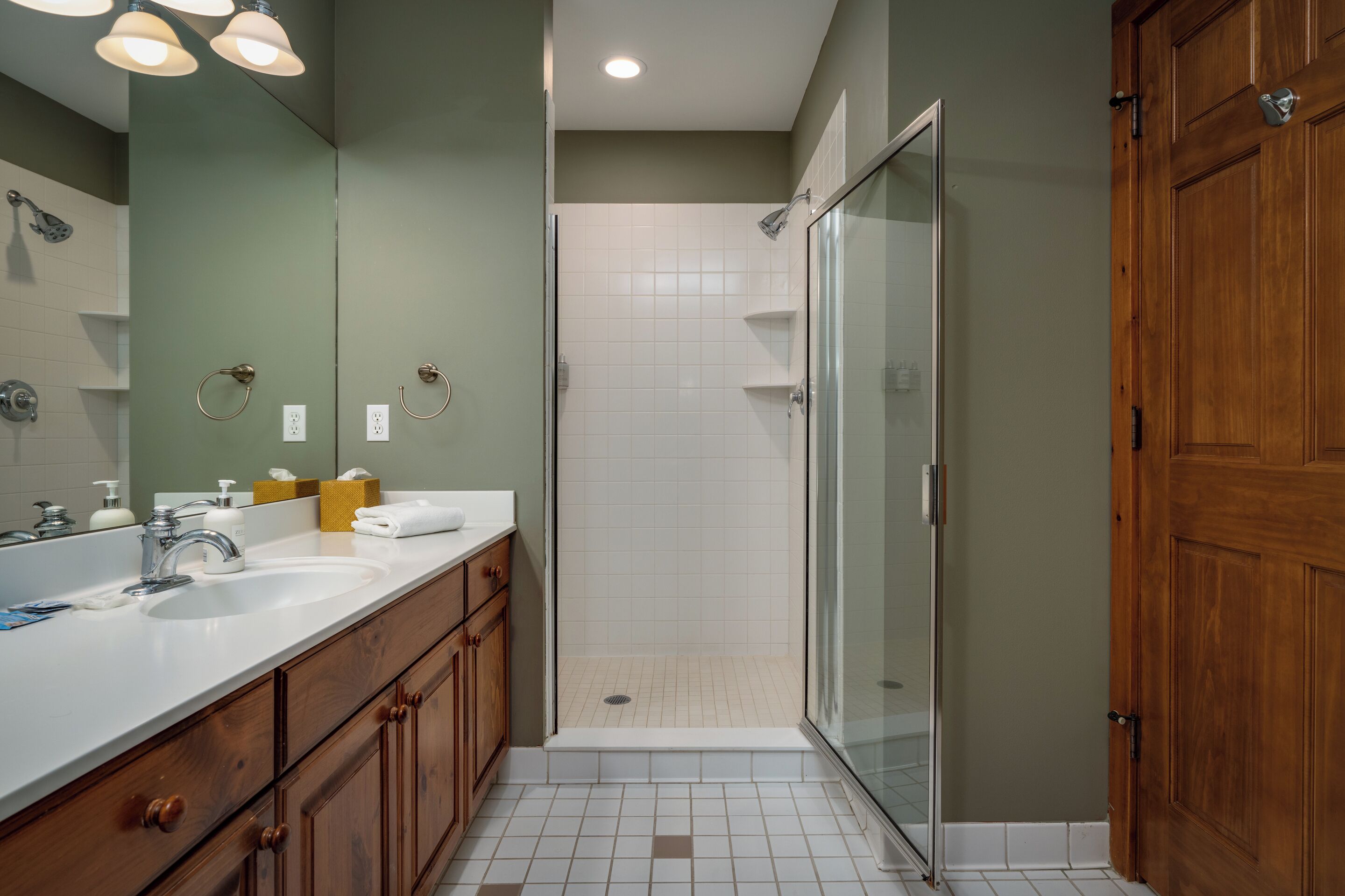 A bathroom with a double sink vanity, a glass shower enclosure, and wooden cabinetry.
