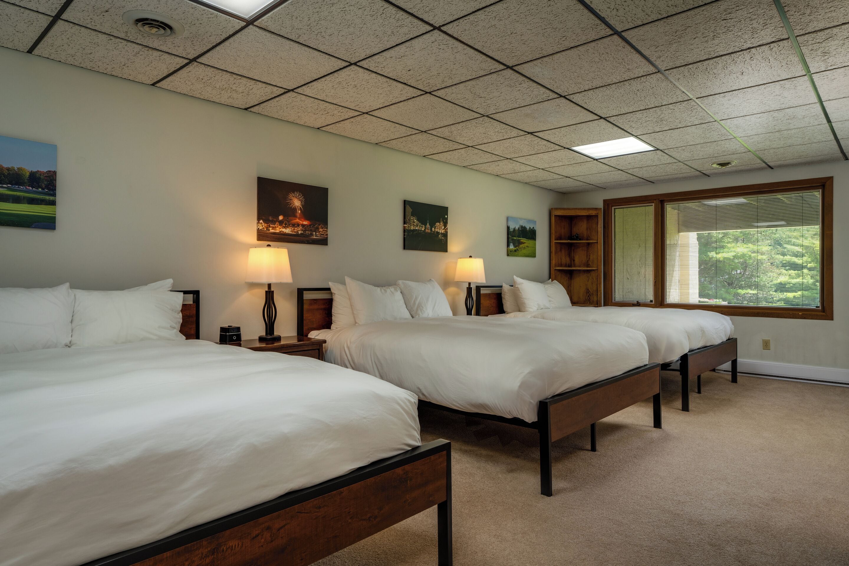 A hotel room with three beds, a large window, and artwork on the walls.