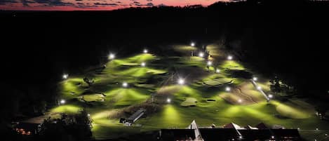 A golf course at night with illuminated holes and a clubhouse.