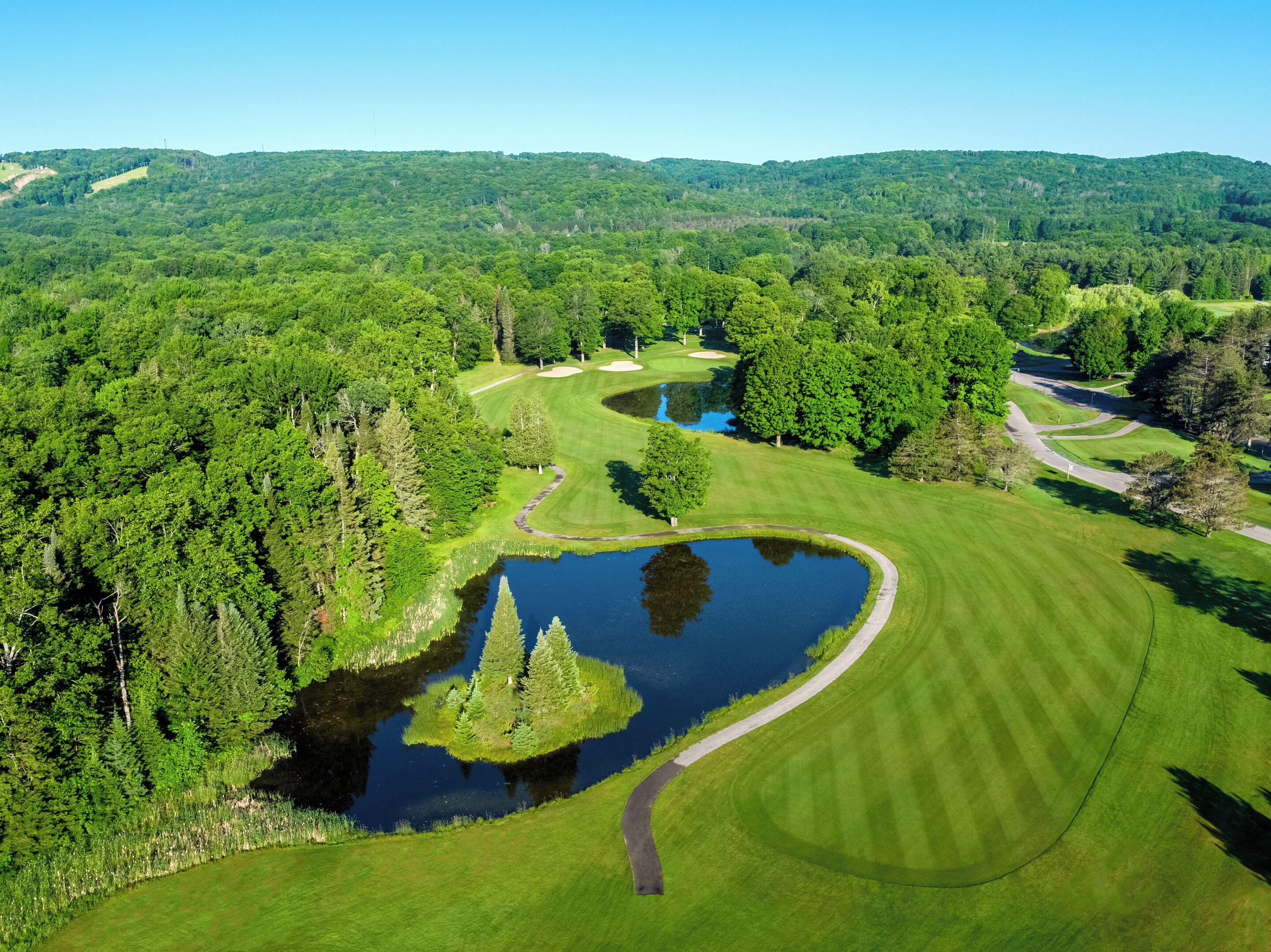 Un parcours de golf avec un étang, entouré d’une forêt dense et de collines.