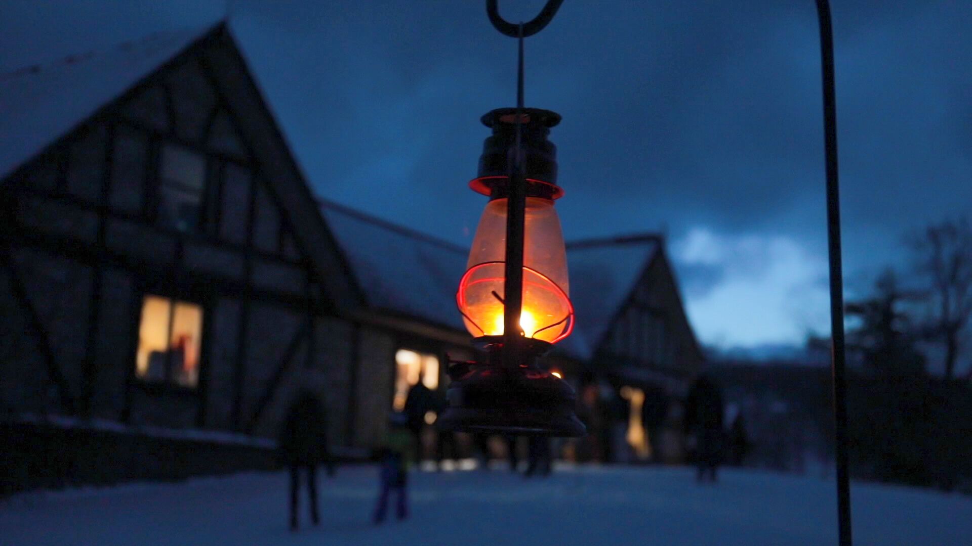 A traditional building with a snow-covered ground, a hanging lantern, and a person in the background.