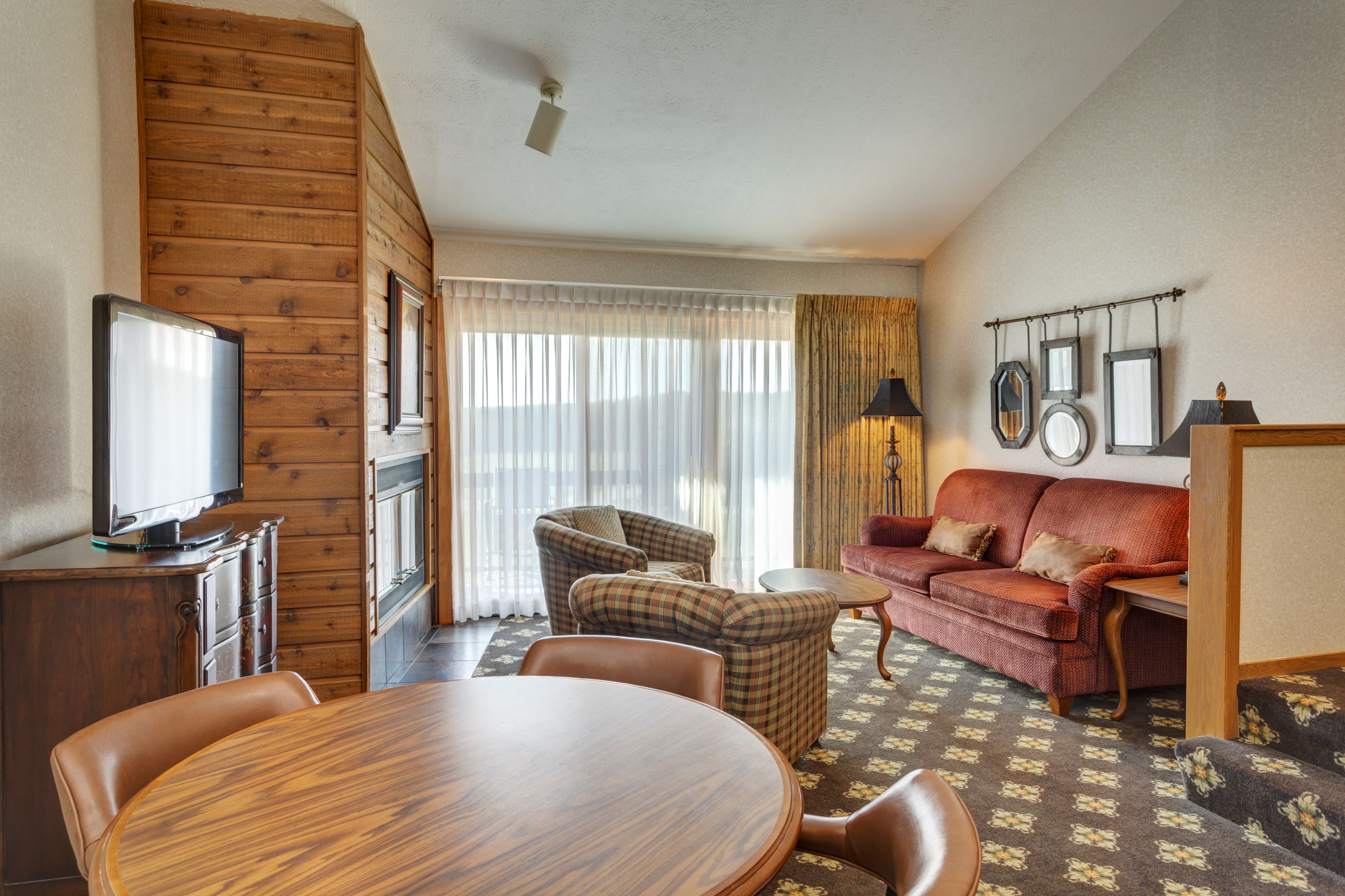 Una habitación acogedora con pared de madera, televisor, sofá rojo, sillón escocés y una mesa de comedor.