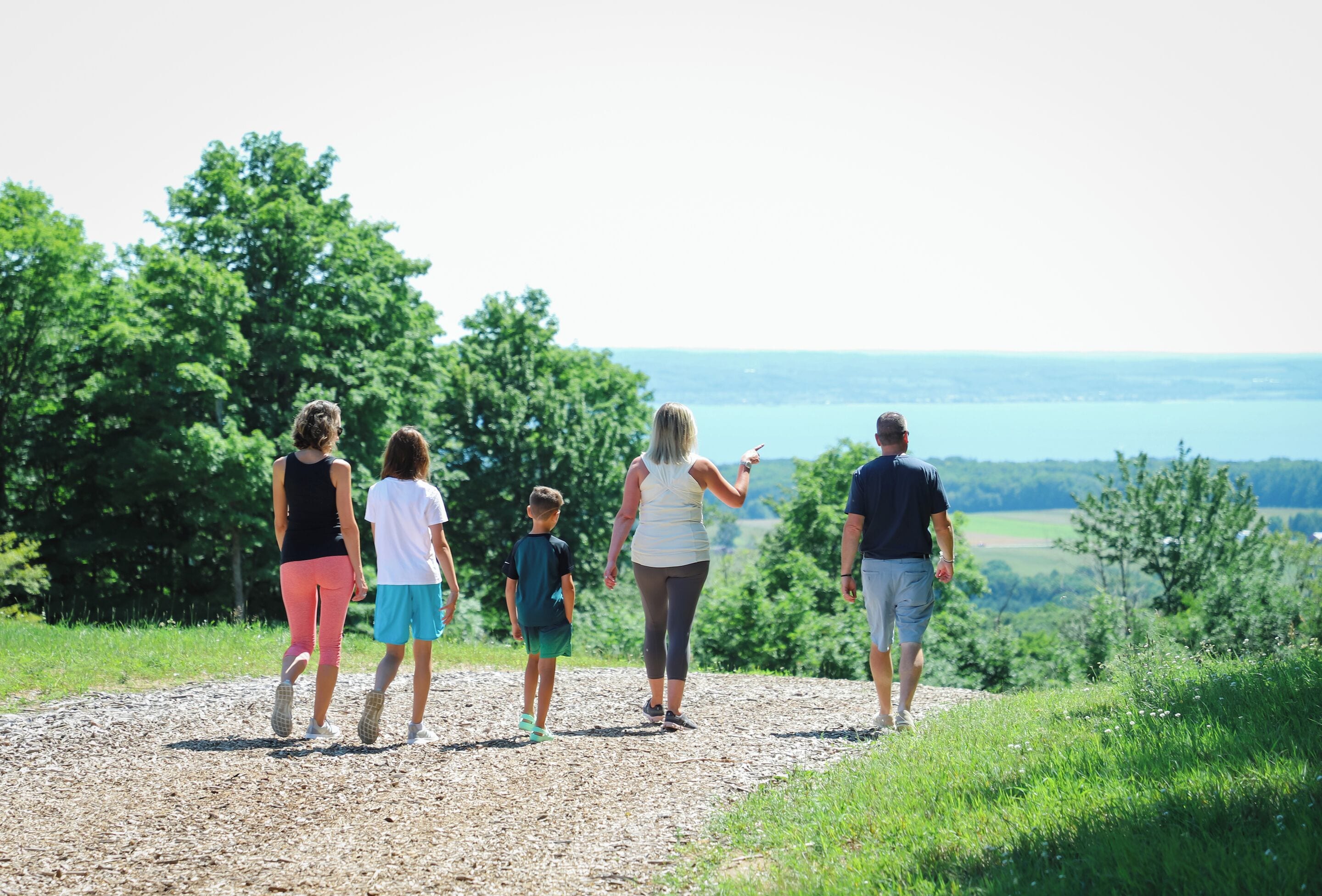 Eine Familie geht auf einem Feldweg, mit Blick auf Bäume und ein Gewässer.