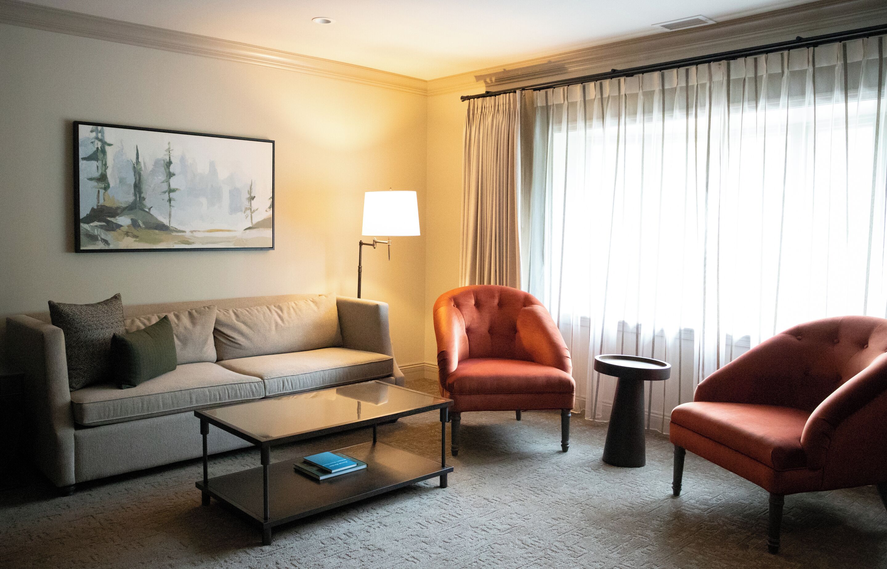 Un salon comprenant un canapé, un fauteuil, une table basse, une lampe et un tableau accroché au mur.