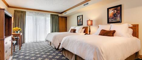 A hotel room with two beds, a desk with a lamp, a dresser, and a painting on the wall.