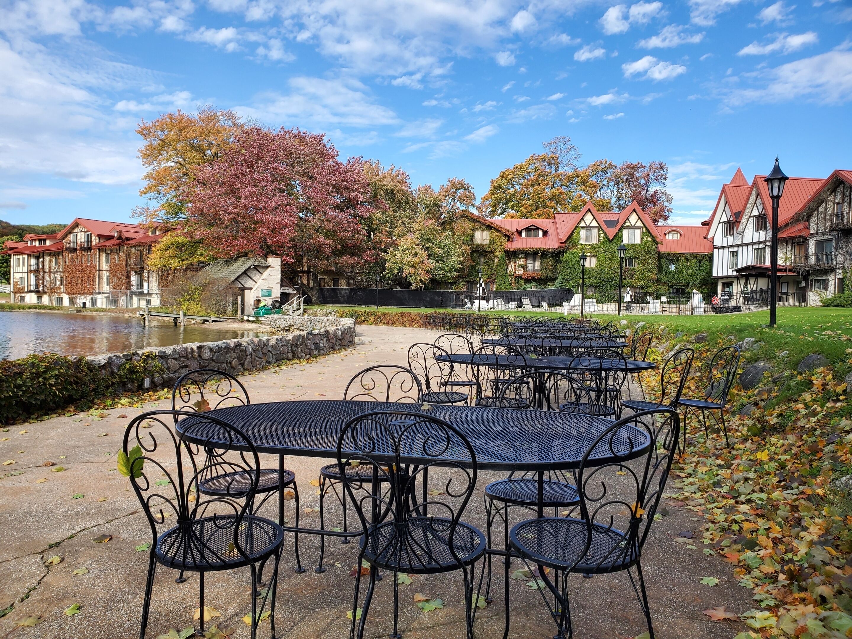 Outdoor seating with tables and chairs, a pond, and buildings with red roofs in the background.